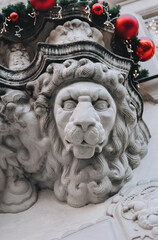 An architectural element is a caryatid under a balcony in the shape of a lion's head. Christmas decorations and fir branches. Lviv, Ukraine.