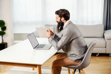 A focused bearded entrepreneur in vest and underwear having conference call at his cozy home.