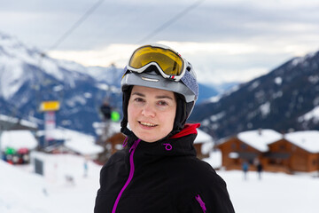Fototapeta na wymiar Smiling female skier wearing helmet and goggles standing on slope of ski resort on winter day 
