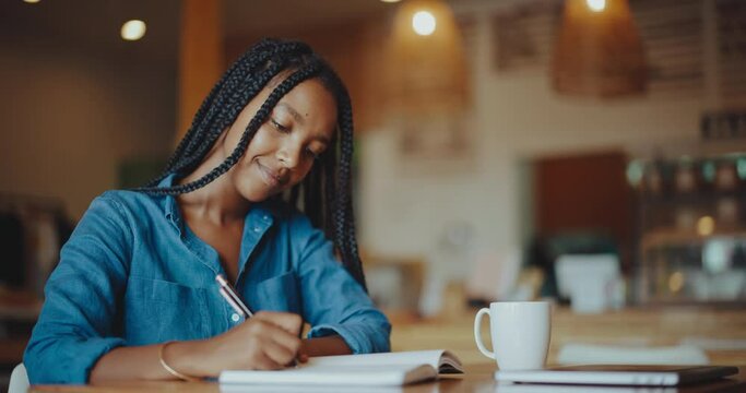 Black college student writing in her notebook, working and relaxing in coffee shop