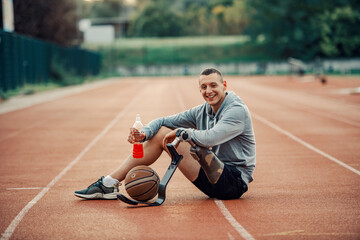 A handicapped basketball player with artificial leg sitting at stadium, drinking refreshment and...