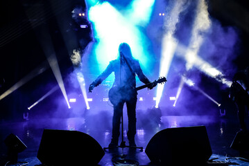 silhouette of a singer vocalist and guitar player performing at a concert in the fog. Dark background, smoke, concert spotlights