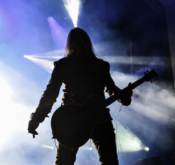 silhouette of a singer vocalist and guitar player performing at a concert in the fog. Dark background, smoke, concert spotlights