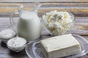 Fresh dairy products, milk, cottage cheese, yogurt, sour cream and butter on a wooden background.