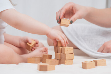 Fototapeta na wymiar Mom is playing with a child, building a house out of wooden eco-friendly cubes, close-up. The concept of early child development through games. Cozy homely atmosphere. Mother's Day, Child's Day