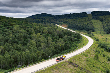 The truck drives along the highway outside the city among the hills. View from afar