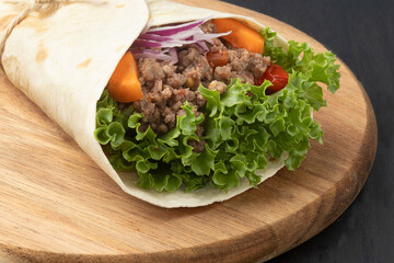 Close up of wrap sandwich of lettuce, onion, tomato, carrot and minced beef.