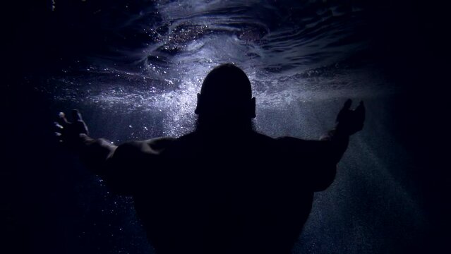 majestic muscular male silhouette inside water of sea or ocean in darkness with sunray, rear view