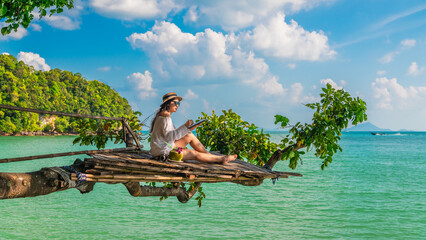 Traveler woman on tree branch using tablet joy nature scenic landscape Railay beach Krabi,...