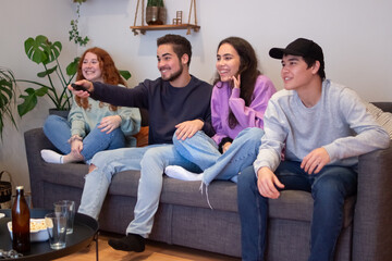 Smiling friends sitting on sofa at home and watching television. Happy and excited men and women having fun on weekend, cheering sports team, switching channels. Entertainment, friendship concept