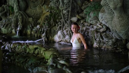 Meditating atmosphere in sacred Bali pond, beautiful woman relaxing in the water, spiritual ornament on walls