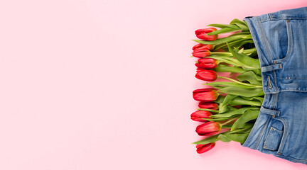 A bouquet of red tulips peeks out of pants or shorts on a pink background. The concept of a healthy...