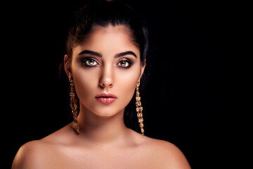 portrait of pretty woman who advertises golden earrings isolated on dark background. Jewelry concept