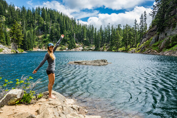 Adventurous athletic woman standing on an alpine lakeshore smiling with her arms spread wide.