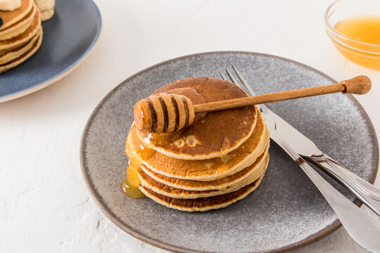 a large stack of homemade pancakes with honey on a gray plate and a white table. traditional American food.