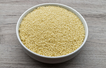 Bowl of raw Couscous isolated on wooden background. Top view.