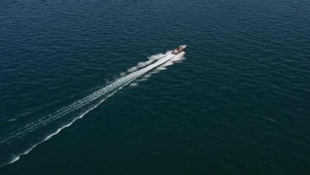 Speedboat in gray color with people fast moving diagonally on dark water aerial view. Boat moves on dark blue water drone view. Modern speedboat in motion on the water.