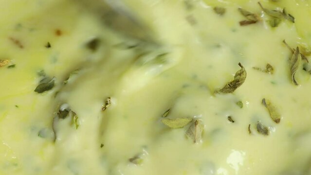 Macro shot of spoon mixing homemade white sauce, mayo, seasoned with parsley. Aioli close up.