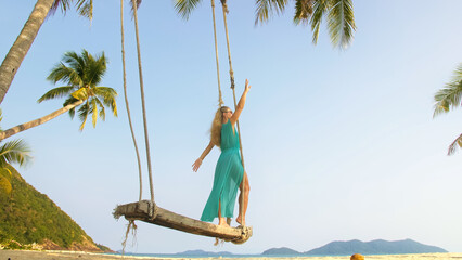 Sexy woman spends her vacation at the seaside. The girl is swinging on a swing. Concept happy...