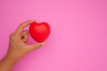 Hand holding a red heart shape on a pink background