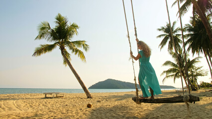 Silhouette woman spends her vacation at the seaside. The girl is swinging on a swing. Concept happy...
