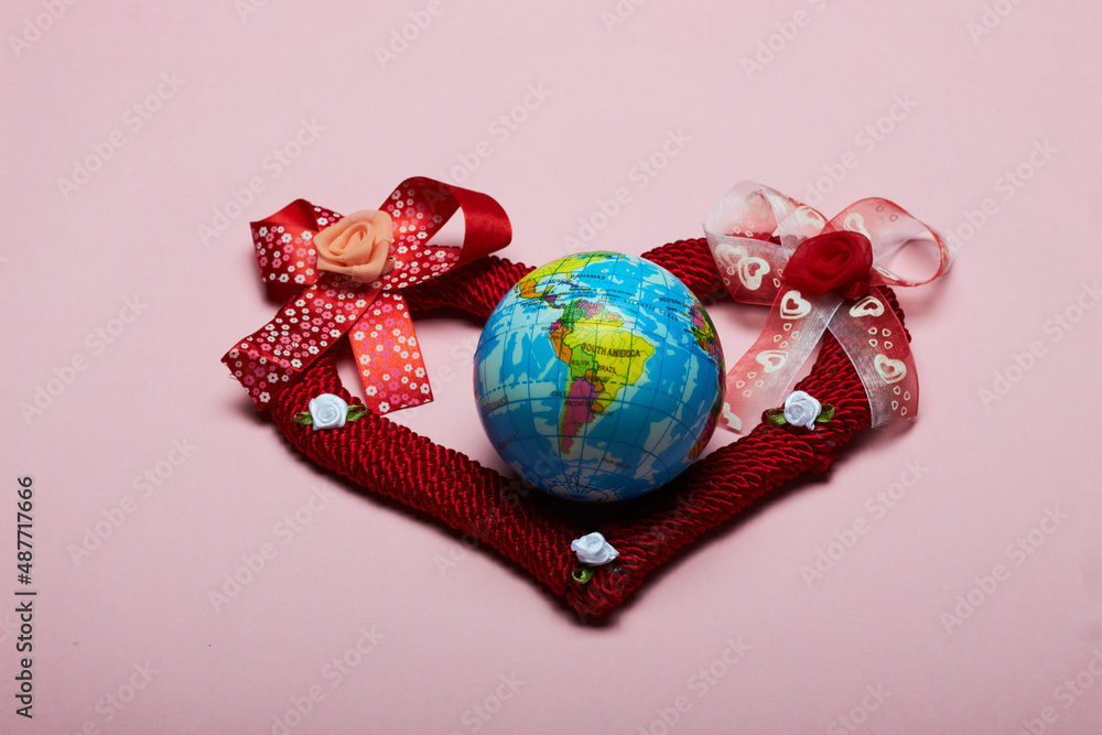Poster a closeup shot of a red heart and a small globe on a pink background with copy space