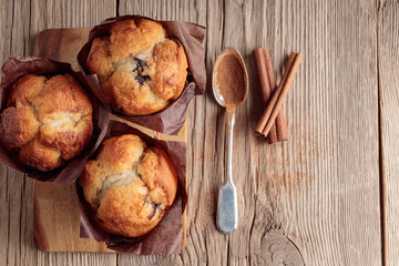 Top view of three homemade delicious muffins and cinnamon on wooden background. Selective focus. With copy space.