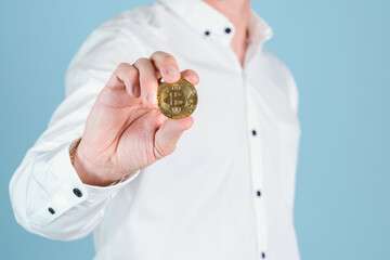 A businessman holds a bitcoin gold coin at arm's length