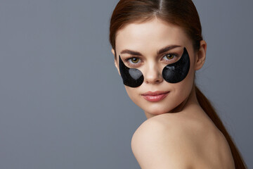 woman eye patches on face bare shoulders skin care Gray background