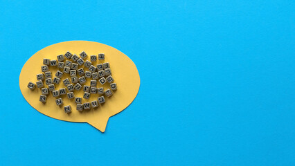 Yellow speech bubble and gold beads of alphabet on blue background with copy space.