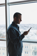 Young business man holding a phone. In an office or business center against the background of large windows of a skyscraper. Work and career, concept