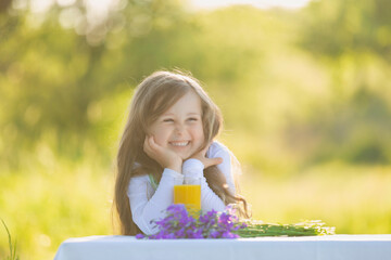 cheerful and smiling girl sits at a table on which there is orange juice