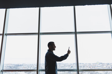 Young business man holding a phone. In an office or business center against the background of large windows of a skyscraper. Work and career, concept