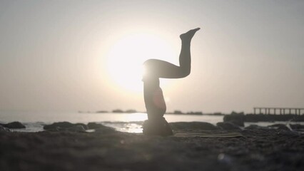 Silhouette afro woman head standing yoga asana on ocean beach during sunrise. Healthy morning workout meditative routine - Powered by Adobe