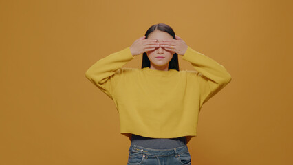 Asian woman covering mouth, eyes and ears in studio, doing three wise monkeys symbolic gesture, not listening to noise and not speaking. Young adult gesticulating serious expression