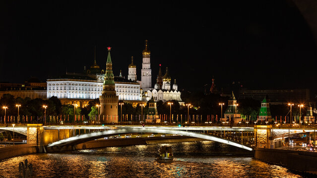 Stadtpanorama Moskau mit Moskwa, Schiffen und Br&uuml;cke im Vordergrund und dem beleuchteten Kreml samt Mauer, T&uuml;rmen, Kirche und Geb&auml;uden bei Nacht