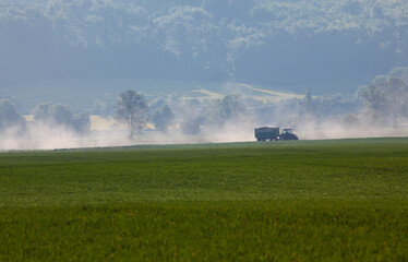 Ein Bauer fährt mit seinem Traktor und einem Anhänger auf einem Feldweg vor einer hügeligen...