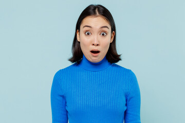 Shocked surprised astonished impressed young woman of Asian ethnicity 20s years old wears blue shirt looing camera keep mouth wide open isolated on plain pastel light blue background studio portrait.