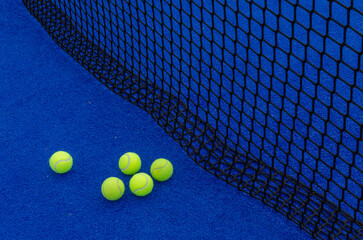 Five paddle tennis balls near the net on a blue paddle tennis court.