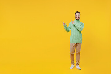 Full body smiling happy fun young man 20s wearing mint knitted sweater point index finger aside on workspace area isolated on plain yellow background studio portrait. People lifestyle fashion concept.