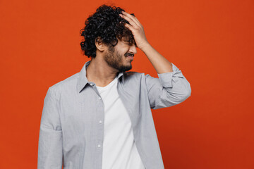 Depressed bored tired frustrated young bearded Indian man 20s years old wears blue shirt put hand on face facepalm epic fail mistaken omg gesture isolated on plain orange background studio portrait.