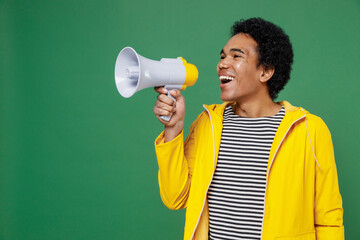 Vivid young black curly man 20s wears yellow waterproof raincoat outerwear hold scream in megaphone...