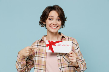 Fototapeta na wymiar Young smiling happy woman 20s in casual brown shirt hold point finger on gift certificate coupon voucher card for store isolated on pastel plain light blue color background. People lifestyle concept.
