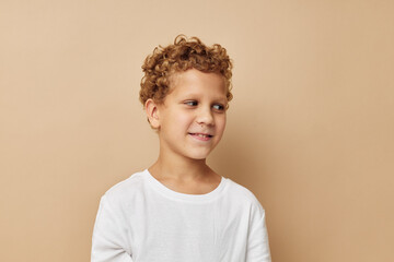 Cheerful boy with curly hair in a white t-shirt beige background