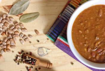 Fototapeta na wymiar Bowl of Chili With Pinto Beans on Table With Peppers and Dry Beans in Background