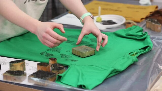 Hand-printed pattern on fabric. Women's hands put a seal on a green T-shirt with acrylic paints for fabric. Ancient traditions. Modern hobbies and creativity