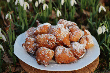 Traditional italian Fritters called Frittelle on a plate in a bunch of Snowdrops flowers