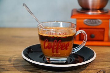Close up photo of milk coffee served in a clear cup and coffee grinder background
