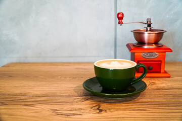Flat White coffee served in a green cup and a traditional coffee grinder background with a negative space composition