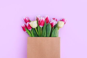 bouquet of colorful tulips in a paper bag on a pink background